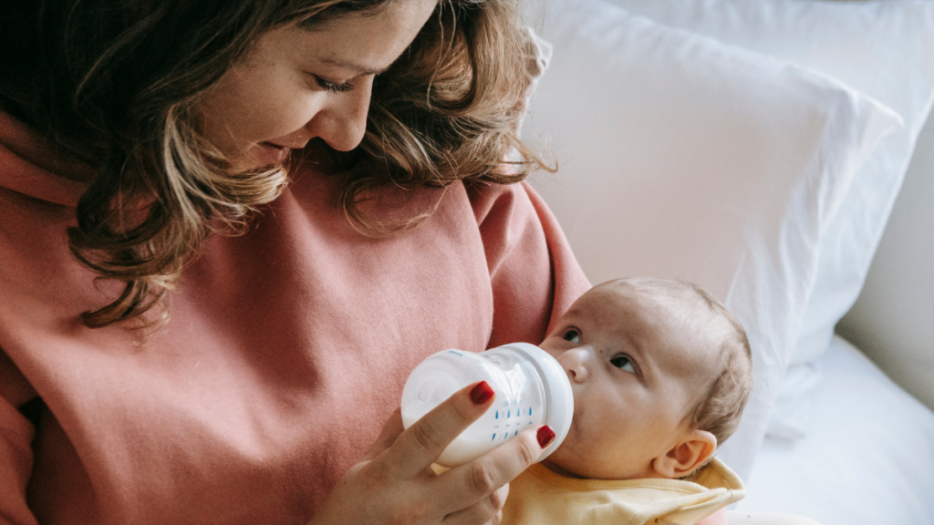 mother feeding a bottle to infant looking up at her